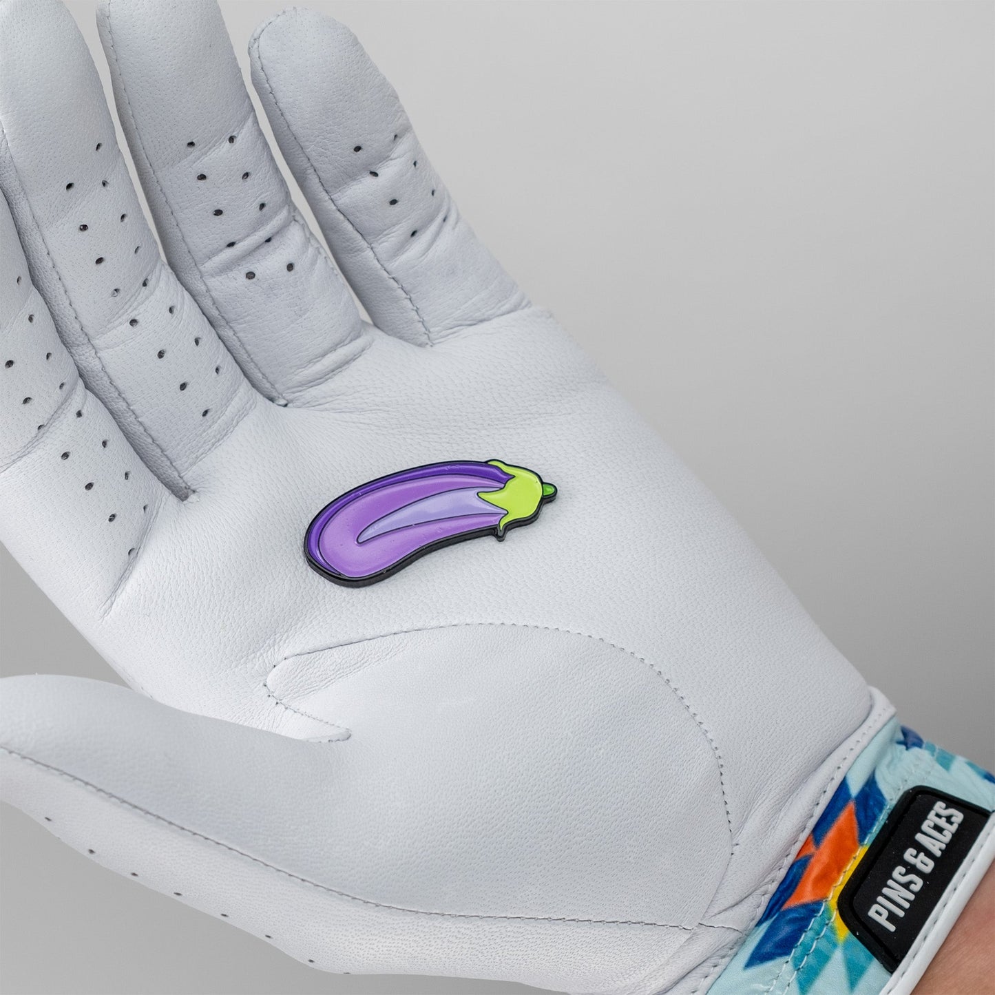Eggplant-shaped ball marker resting on a golfer's gloved hand, showcasing a fun and unique accessory for the course.