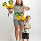 A child and adult hold colorful TMNT-themed golf headcovers, both wearing matching playful shirts, ready for a fun day on the course.