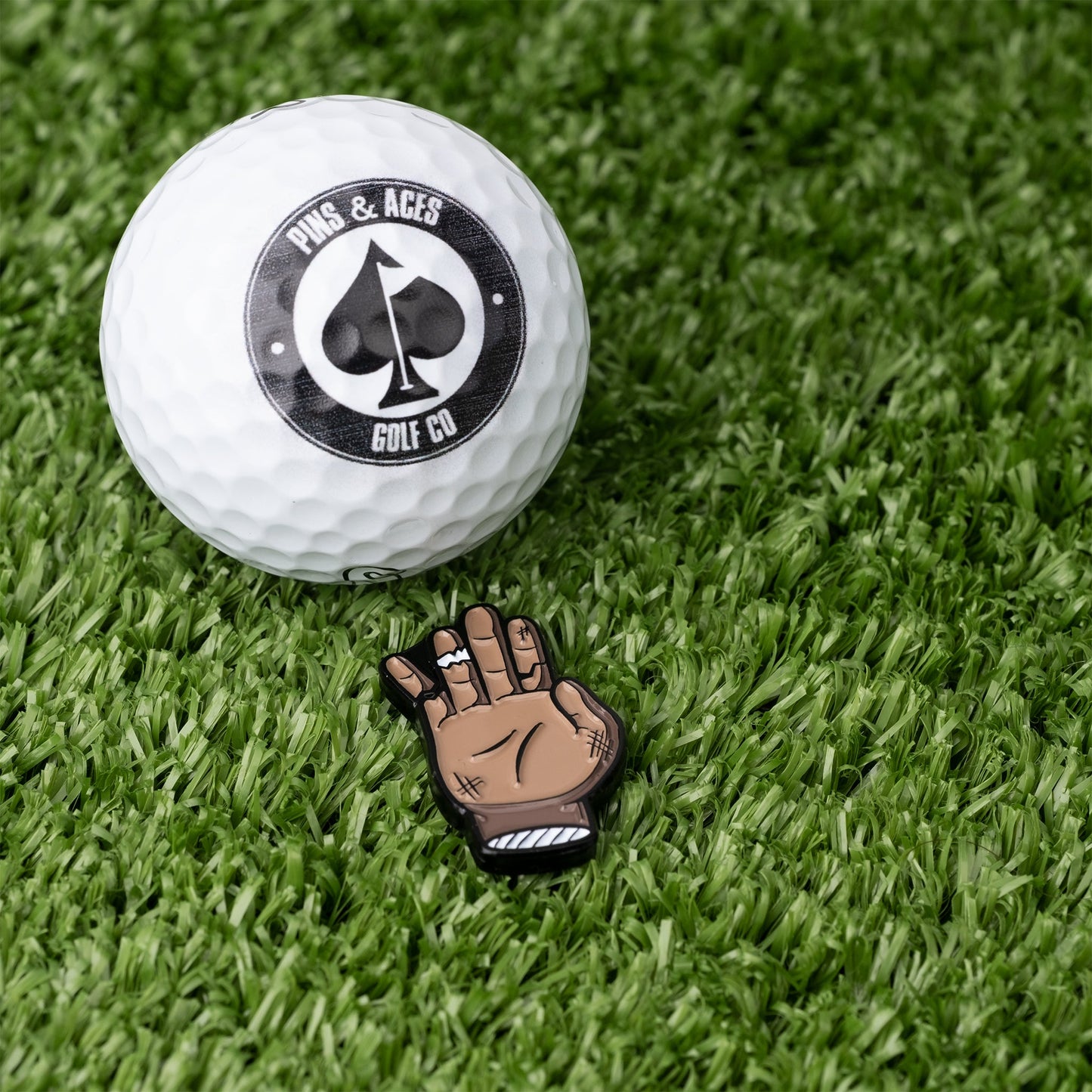 Chubs Hand Ball Marker features a playful hand design next to a golf ball on green turf, perfect for stylish golfers.