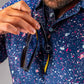 A golfer wearing a blue splatter polo shirt holds sunglasses near the collar, showcasing a stylish and bold golf look.