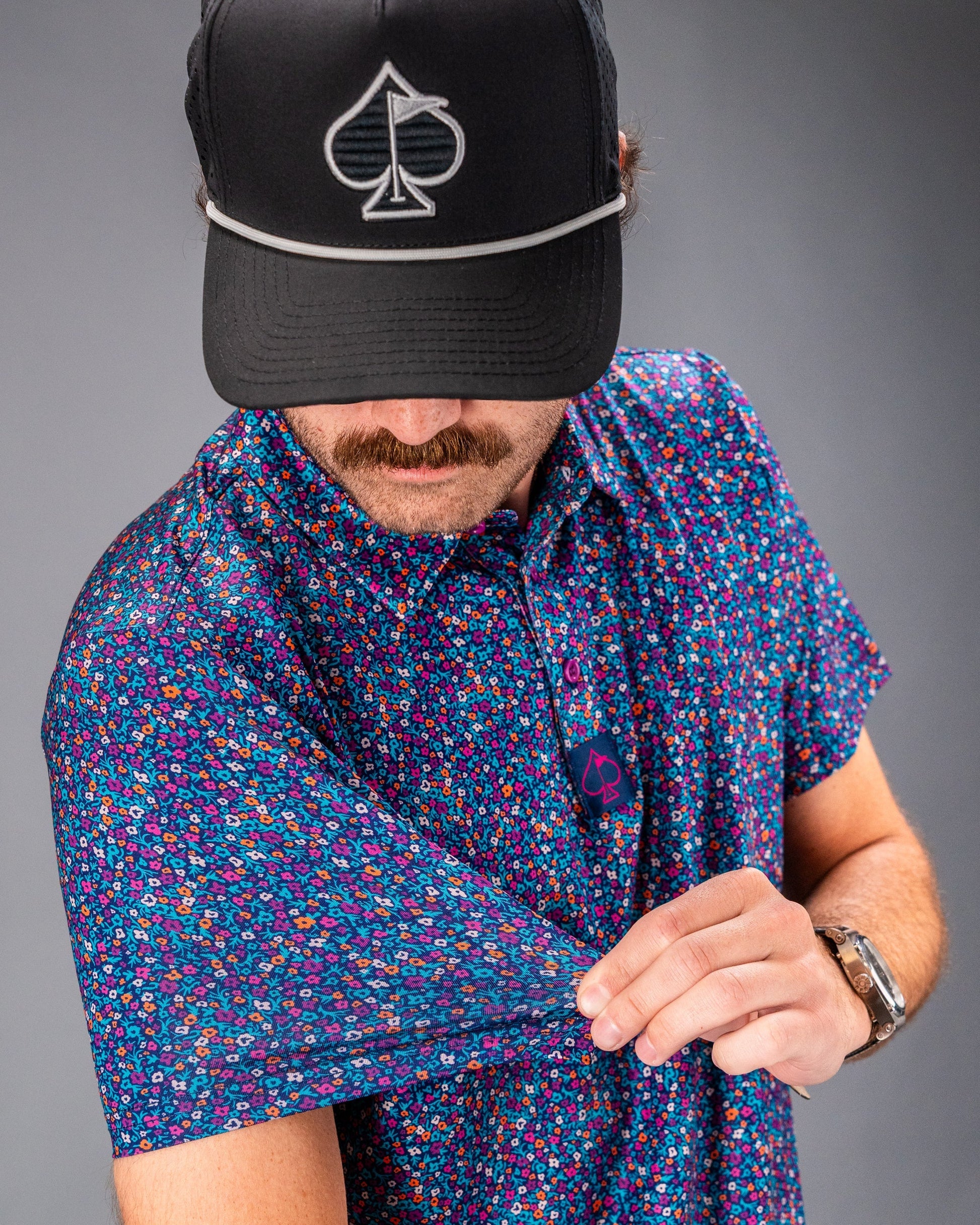 A golfer showcases the Lavender Flower Power polo, featuring a vibrant floral pattern, while adjusting the sleeve.