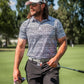 Stylish golfer wearing a Fragment Black polo shirt and cap, holding a golf club on a sunny course.