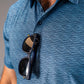 Blue golf polo with a textured squiggle pattern, featuring sunglasses casually placed on the collar.