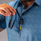 A golfer holds sunglasses while wearing a blue patterned polo shirt with a logo on the collar, showcasing stylish golf apparel.