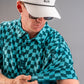 A golfer adjusts the sleeve of a bold wavy checkered polo shirt in teal and black, showcasing its unique pattern.