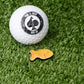 Gold fish cracker ball marker beside a golf ball, showcasing its unique design.