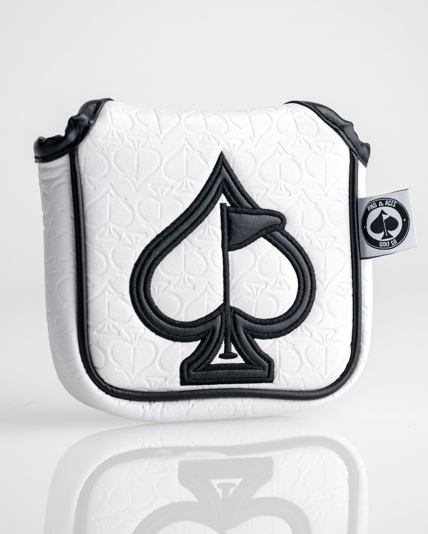 White golf headcover with black spade and flag embroidery, textured background, and "Pins & Aces" logo tag.