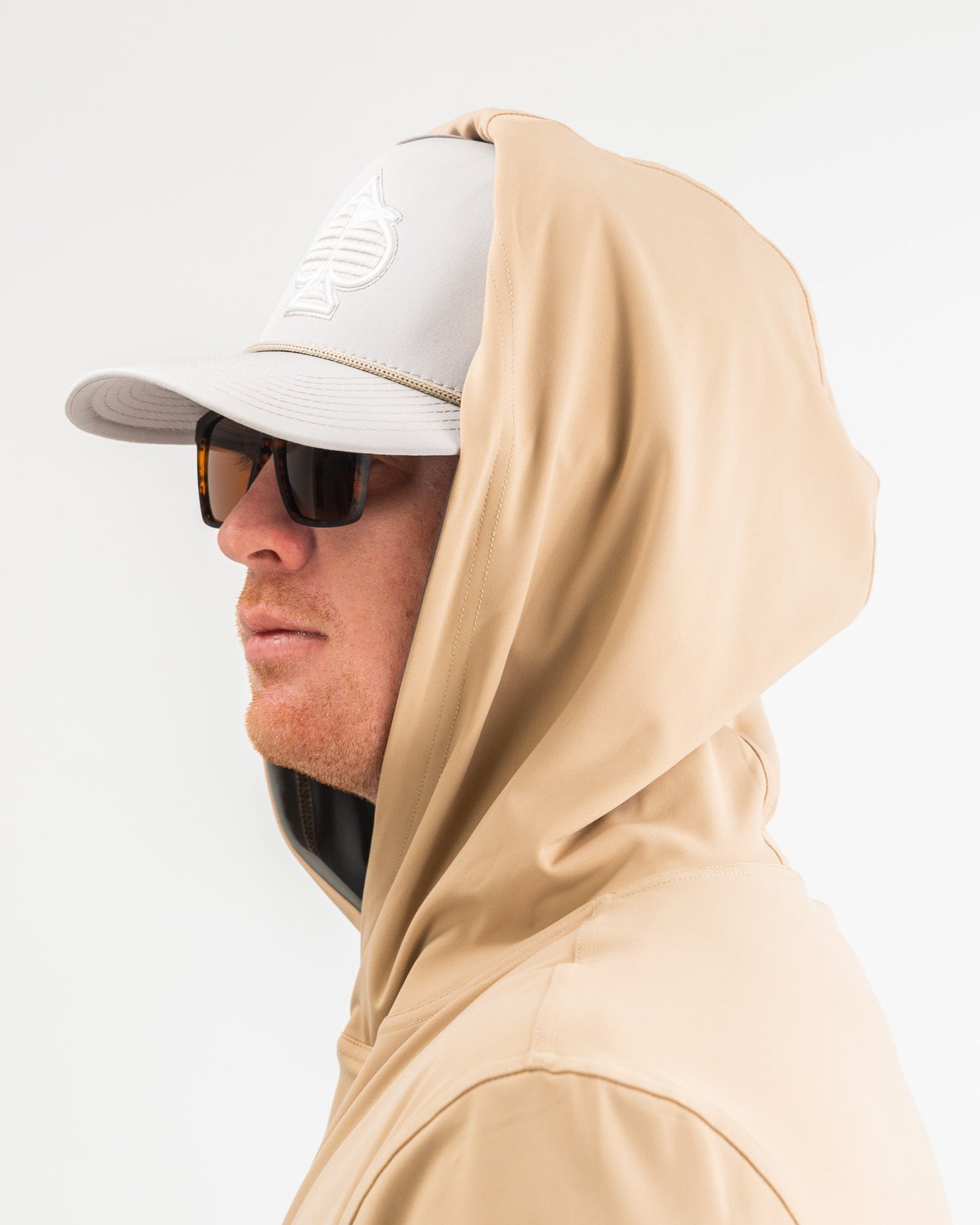 Performance golf hoodie in sand color, featuring a relaxed fit and a hood, paired with a cap and sunglasses.
