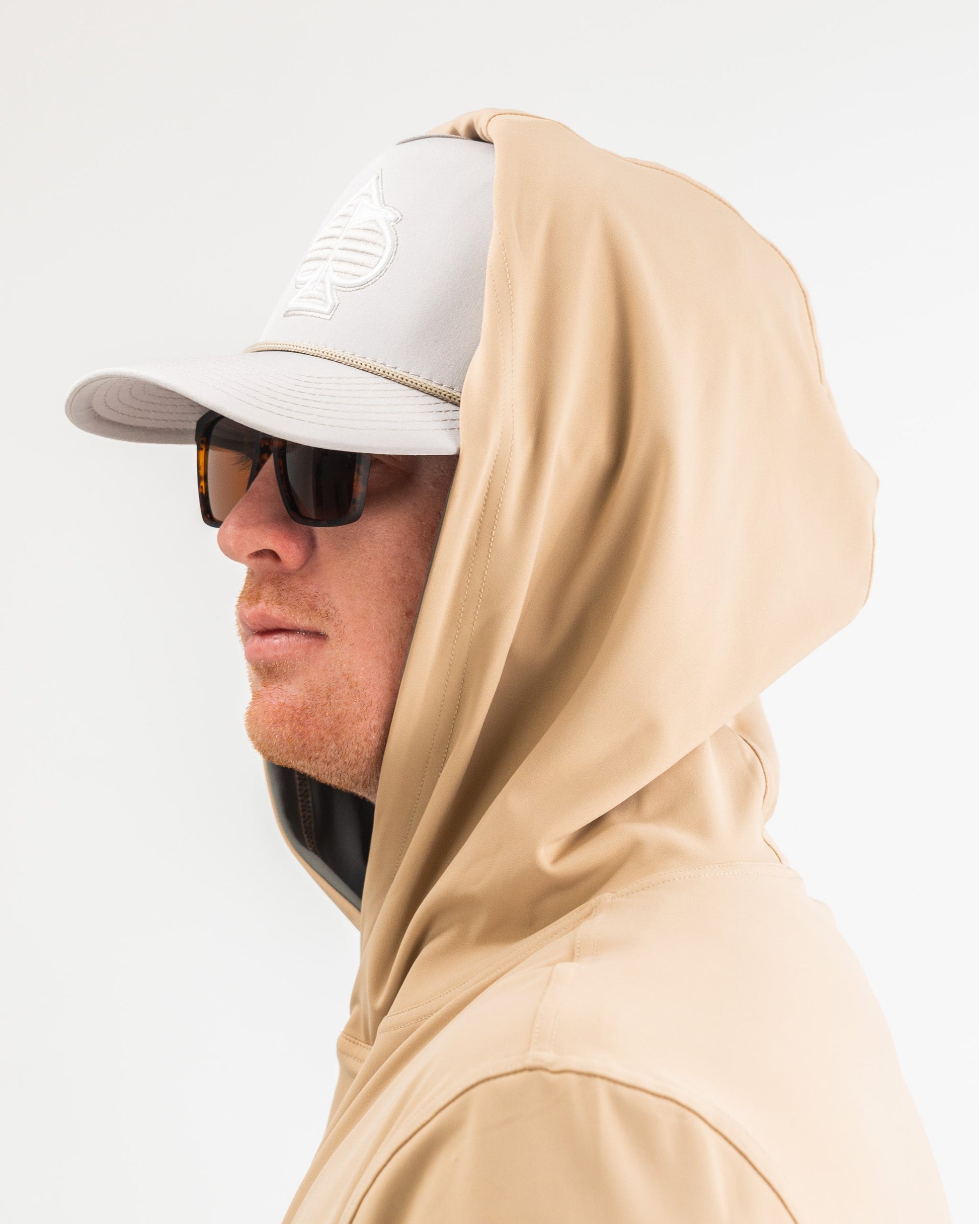 Performance golf hoodie in sand color, featuring a relaxed fit and a hood, paired with a cap and sunglasses.