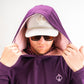 Man wearing a houndstooth raspberry performance golf hoodie with a hood up, sunglasses, and a cap, showcasing a stylish look.