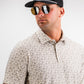Stylish man wearing the Player Preferred™ Polo in Old Fashioned print, paired with sunglasses and a cap, showcasing bold golf fashion.