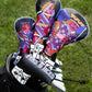 Colorful Ace of Spades blade putter covers in a golf bag on grass, featuring intricate, vibrant designs of playing card royalty in various colors, with the text "Pins & Aces” visible.