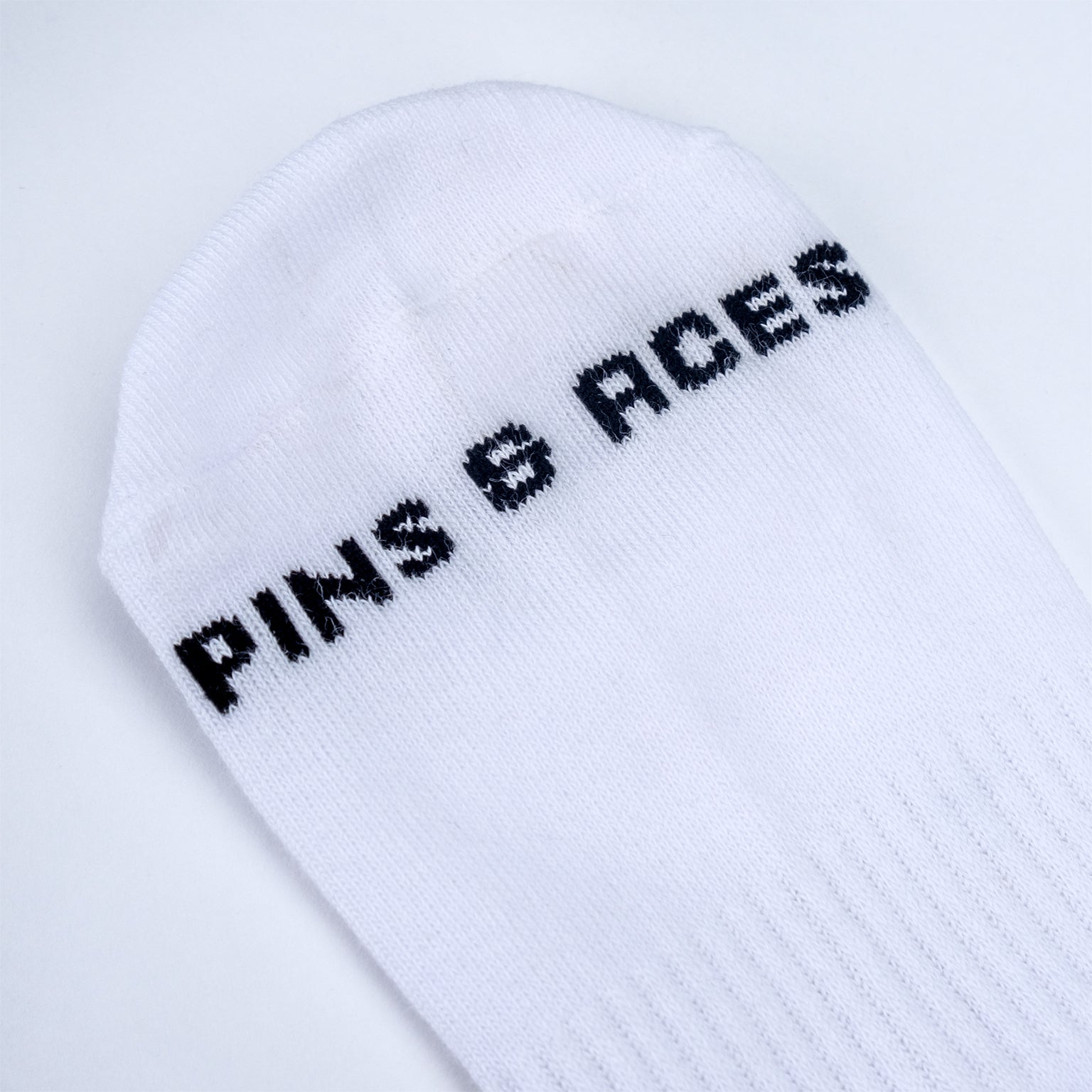 White crew socks featuring "Pins" lettering in black on the side.