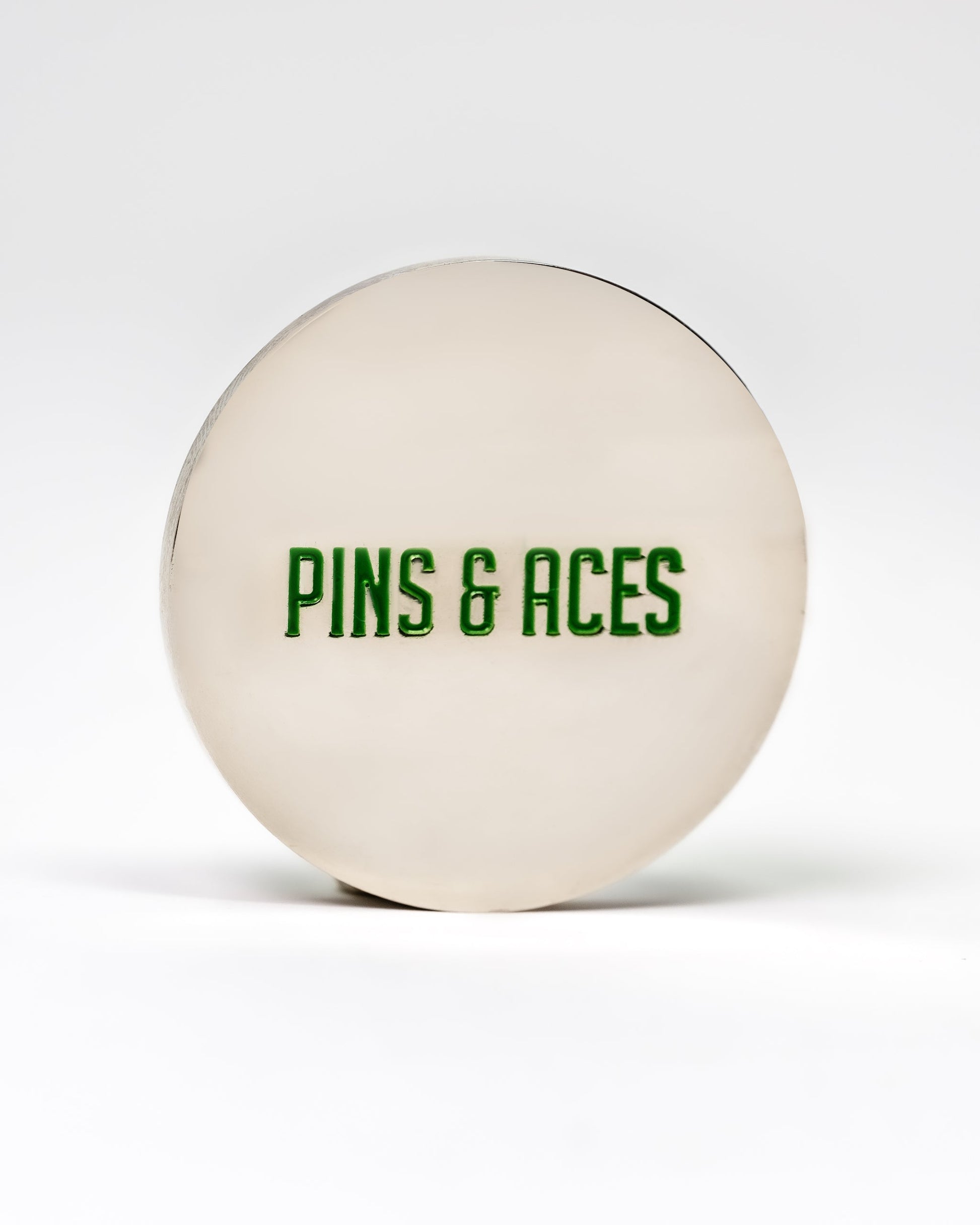 Alt text: "6 Milly - Wintergreen Ball Marker featuring a large, white, circular design with 'PINS & ACES' printed in green font centered on the surface."