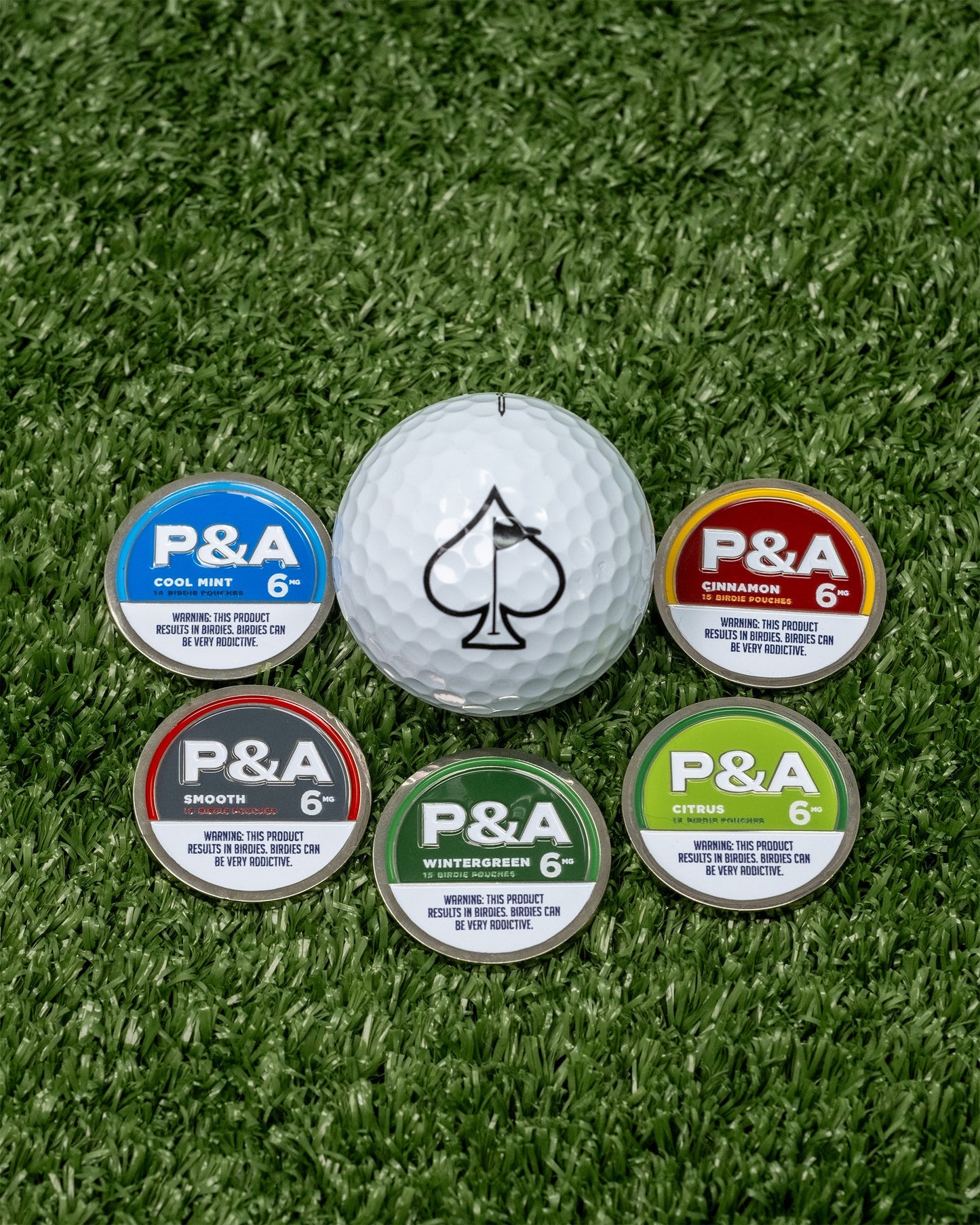 "Six colorful golf ball markers arranged around a white golf ball on green grass.